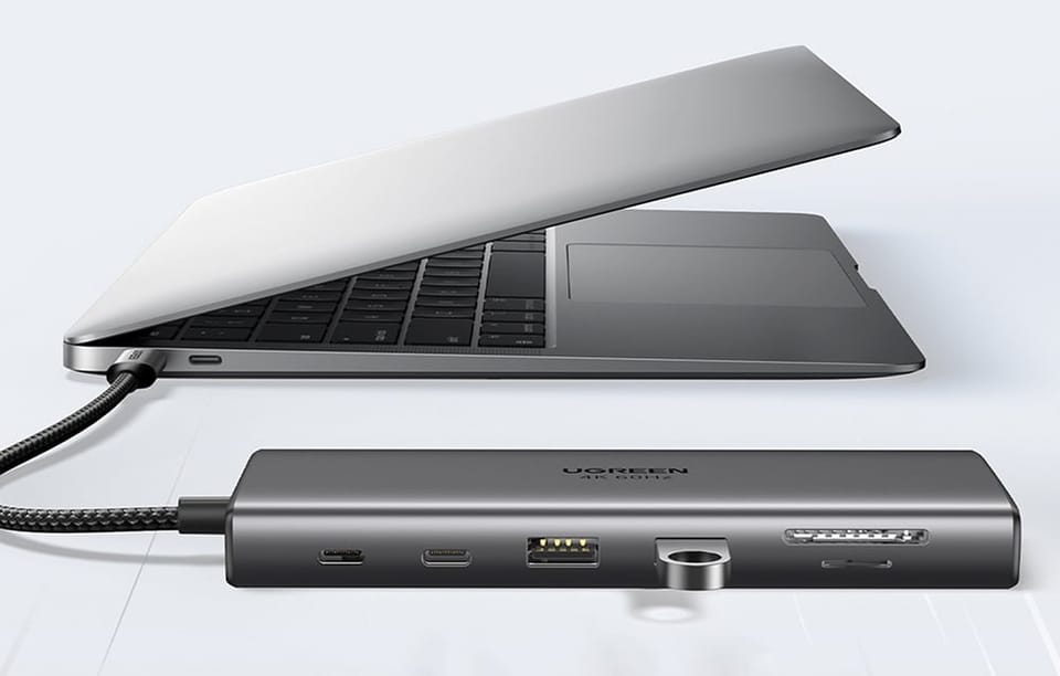 Srebrny hub z podłączonym pendrivem podpięty do laptopa na szarym tle