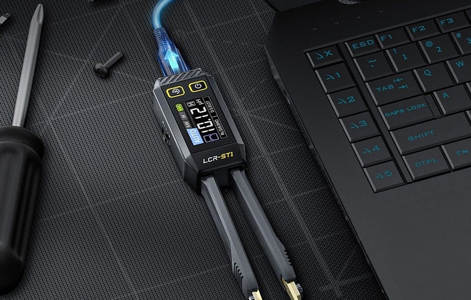 Elektroniczna pęseta pomiarowa podłączona do laptopa leży na czarnej macie obok śrubokręta i śrub.