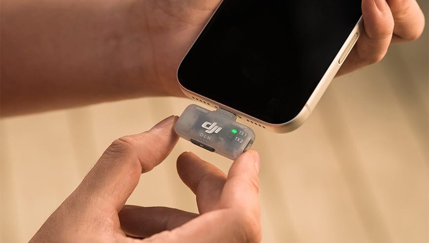 Dłoń podłącza półprzezroczysty odbiornik z zestawu DJI Mic Mini 2 do dolnego portu smartfona
