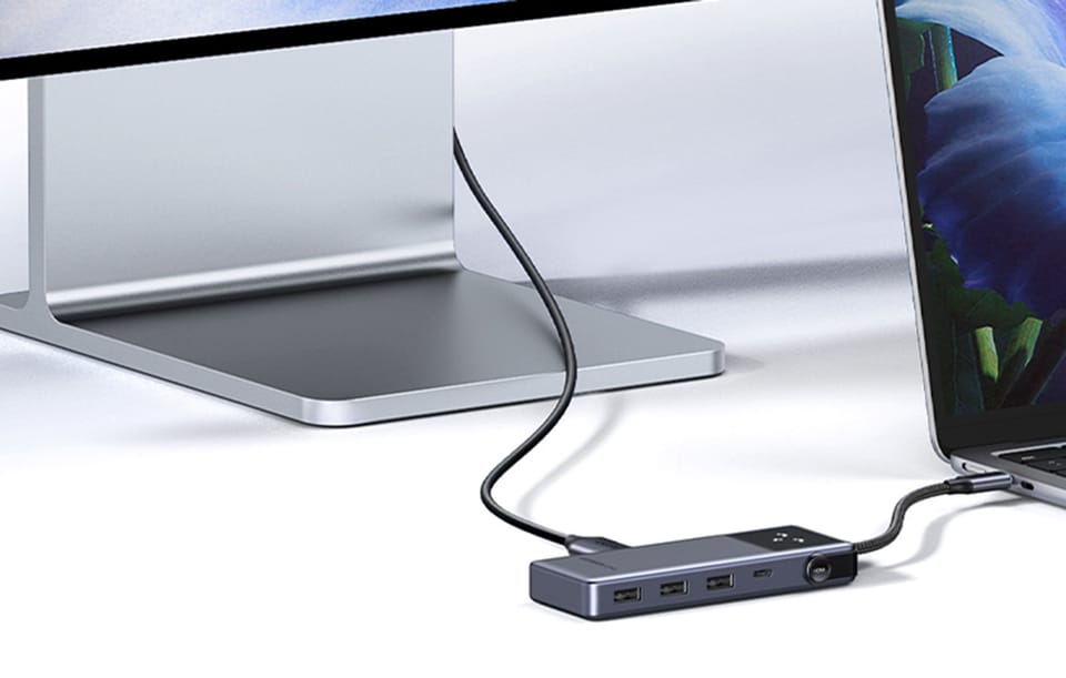 Hub USB z kilkoma portami podłączony do laptopa i monitora na jasnym biurku.