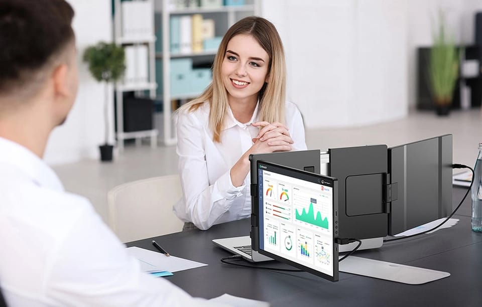 Kobieta w biurze rozmawiająca z mężczyzną, a obok niej laptop z dwoma rozsuwanymi ekranami wyświetlającymi wykresy