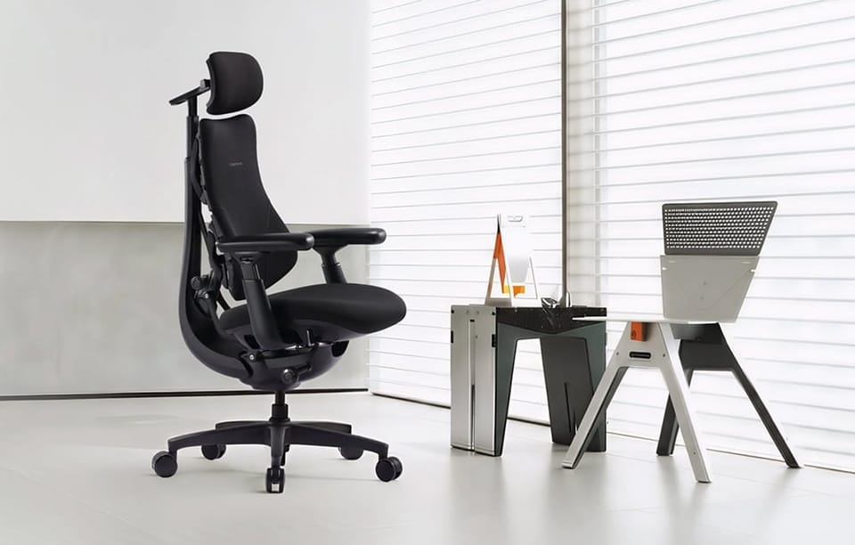 Czarny ergonomiczny fotel biurowy z zagłówkiem stoi w jasnym pomieszczeniu obok nowoczesnego stolika i krzesła