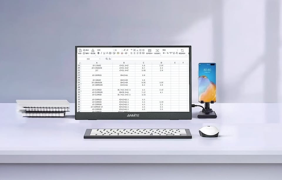 Monitor wyświetlający arkusz kalkulacyjny na biurku z klawiaturą, myszką i smartfonem.