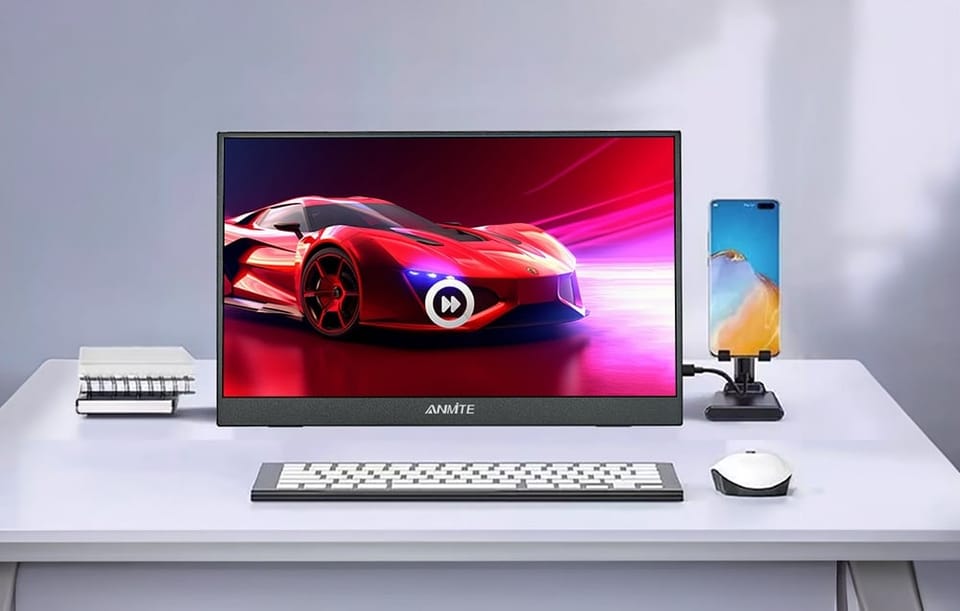 Monitor na biurku wyświetlający czerwone auto, obok klawiatura, myszka i telefon na stojaku.