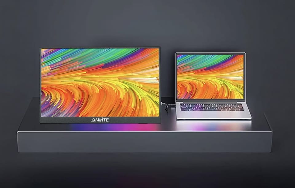 Duży monitor przenośny podłączony przewodem do mniejszego otwartego laptopa na ciemnym podwyższeniu.