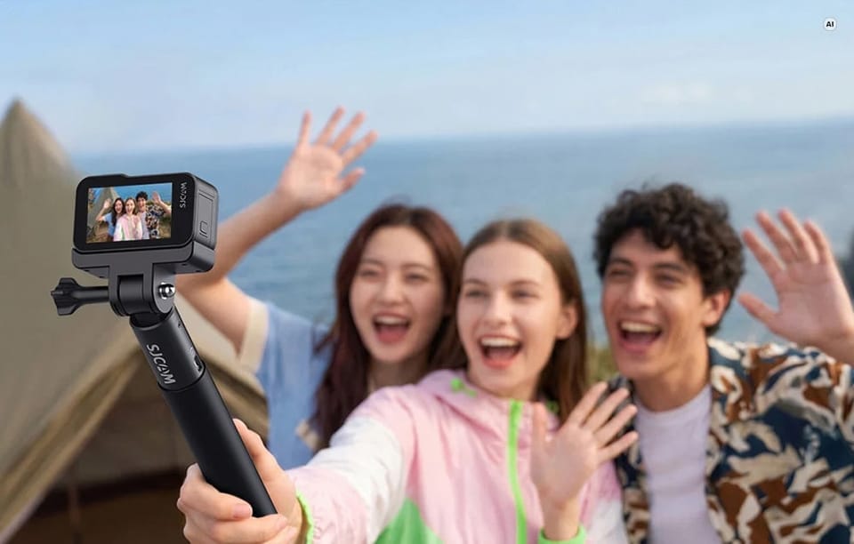 Grupa roześmianych znajomych robiąca selfie przy użyciu kamery sportowej SJCAM na kijku.