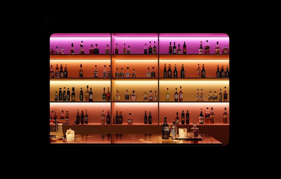 Barowa półka z alkoholami oświetlona kolorowymi taśmami LED w odcieniach fioletu, pomarańczy i złota