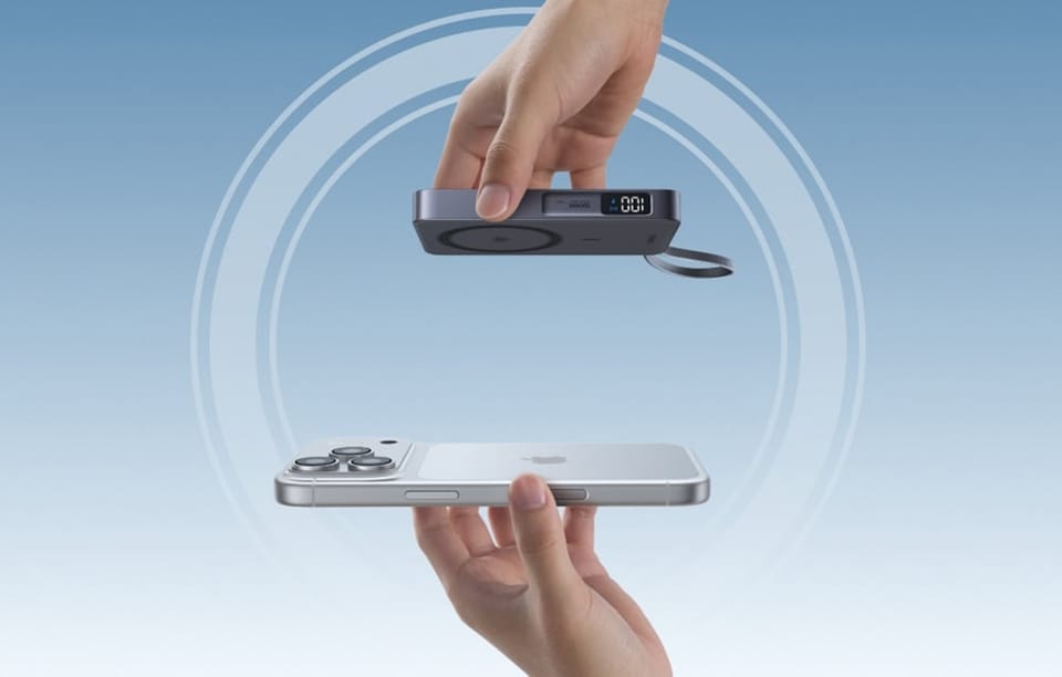 Dwie dłonie zbliżające do siebie smartfon Apple iPhone oraz szary powerbank indukcyjny Ugreen z wyświetlaczem LED