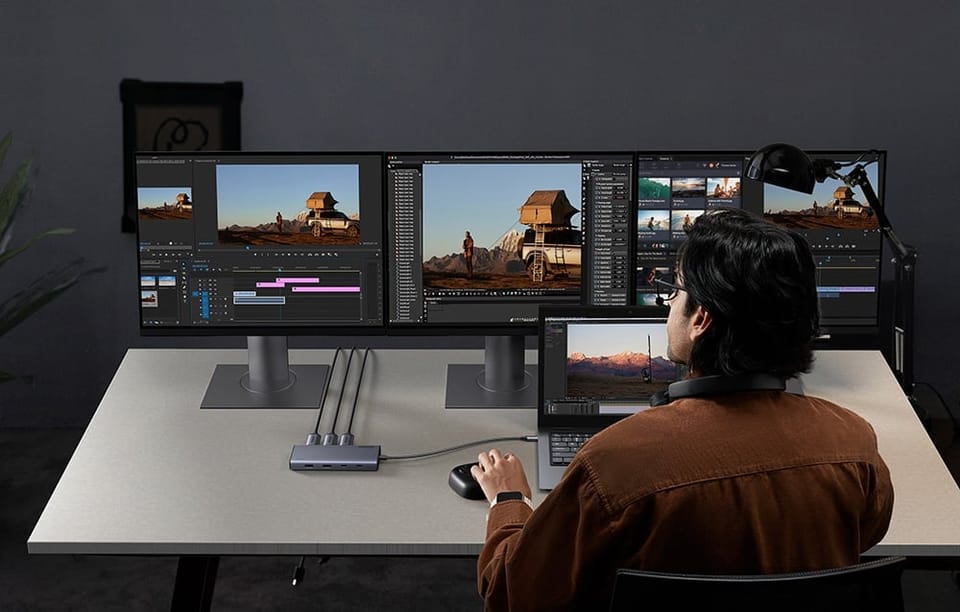 Mężczyzna edytujący wideo na laptopie i trzech monitorach podłączonych przez hub UGREEN.