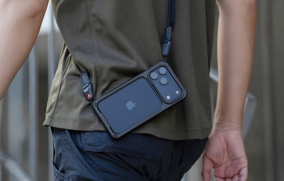 Telefon w czarnej klatce ochronnej przypięty do paska na ramieniu, przewieszony na boku osoby w zielonej koszulce.
