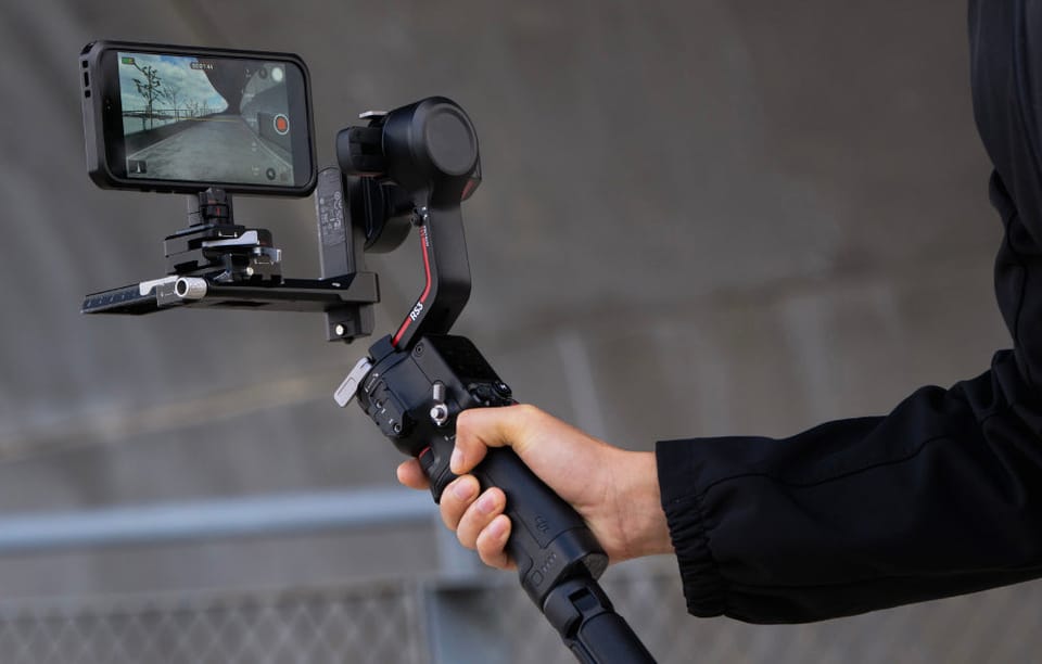 Dłoń trzymająca gimbal z zamontowanym telefonem w klatce ochronnej podczas nagrywania wideo.